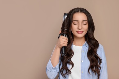 Photo of Beautiful woman using curling hair iron on beige background. Space for text