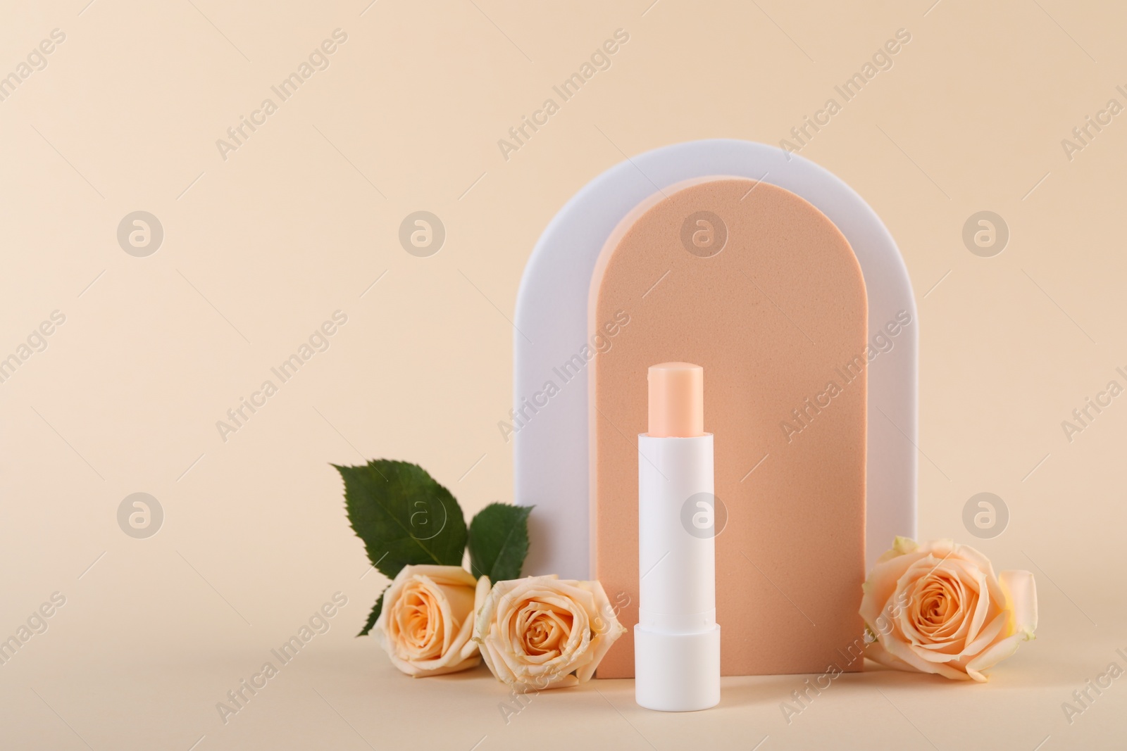 Photo of Stylish presentation of lip balm with rose flowers on beige background, space for text