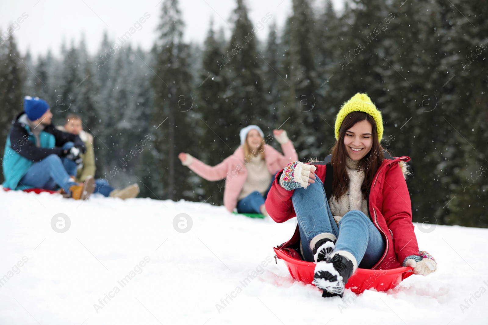 Photo of Happy friends sliding on sleds outdoors. Winter vacation