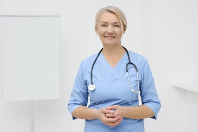 Professional doctor wearing uniform near flipchart in clinic