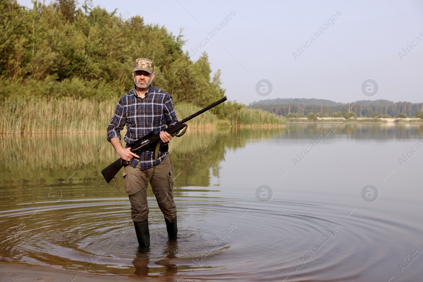 Photo of Man with hunting rifle near lake outdoors. Space for text