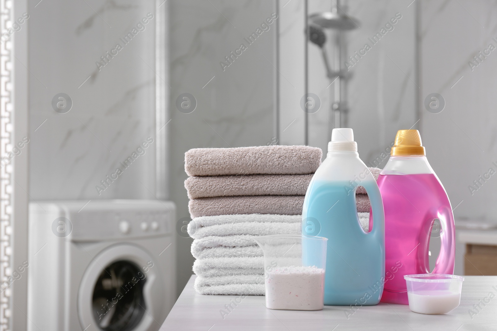 Photo of Stack of folded towels and detergents on white table in bathroom