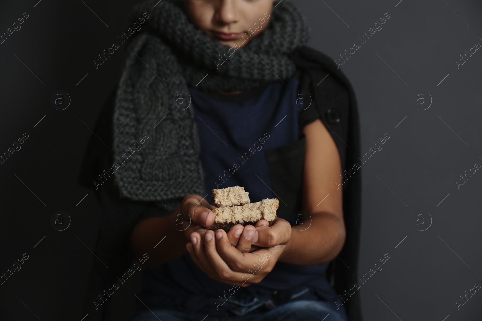 Photo of Poor boy with pieces of bread on dark background, focus on hands