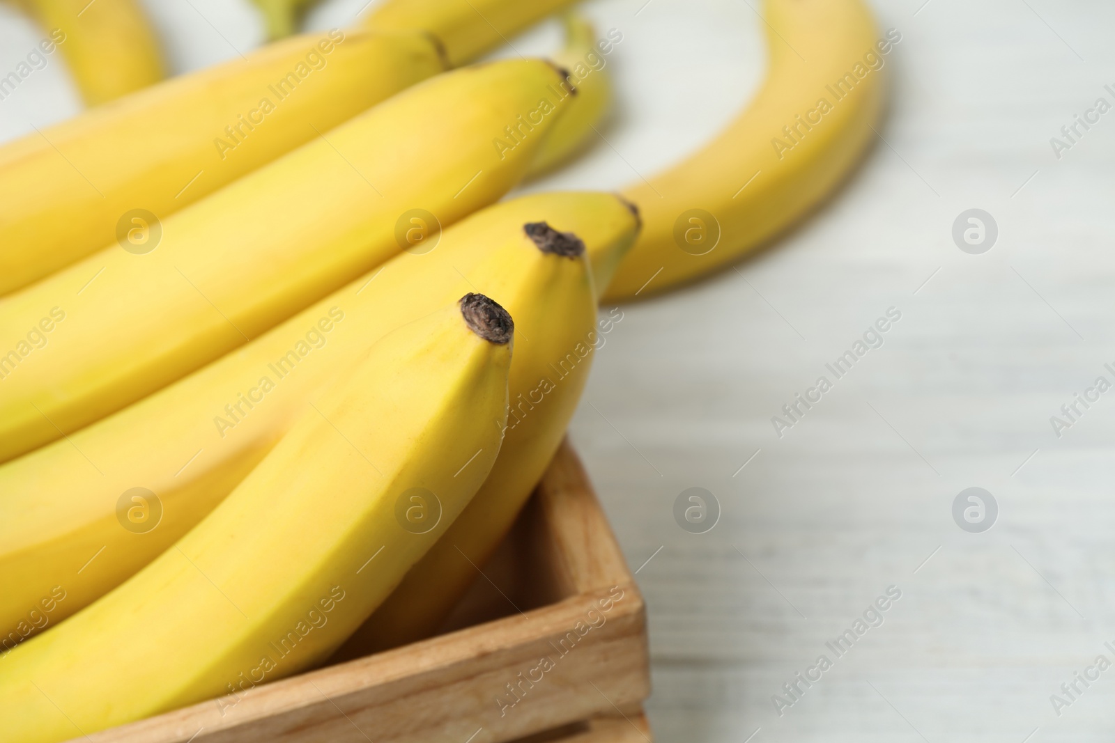 Photo of Ripe yellow bananas and crate on white wooden table, closeup. Space for text