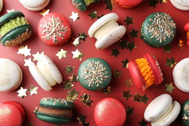 Photo of Beautifully decorated Christmas macarons and confetti on red background, flat lay