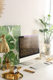 Photo of Modern workplace with computer and golden decor on desk near wall. Stylish interior design