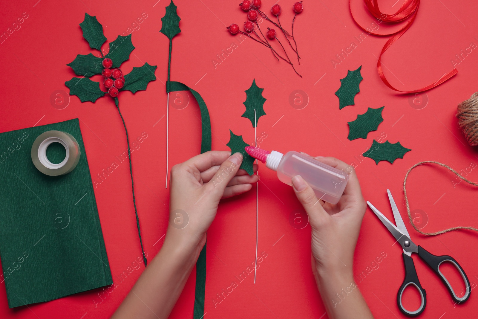 Photo of Woman making mistletoe branch on red background, top view