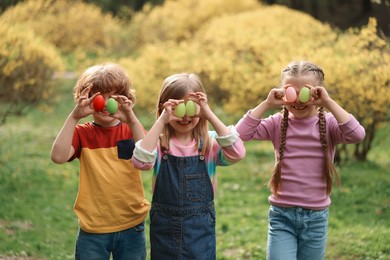 Photo of Easter celebration. Little children covering eyes with painted eggs outdoors