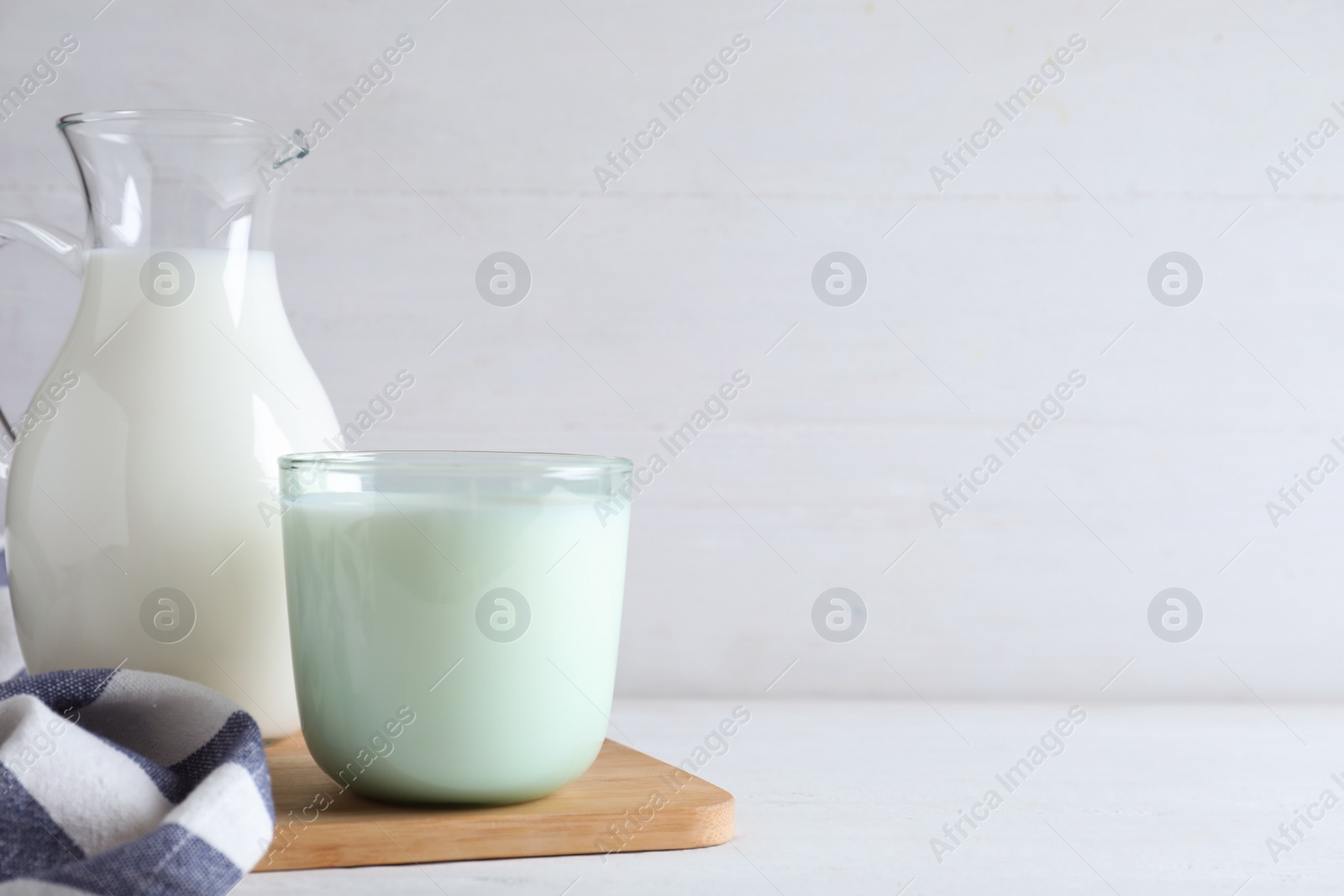 Photo of Jug and glass with fresh milk on white wooden table. Space for text