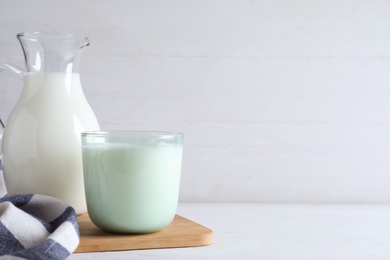 Photo of Jug and glass with fresh milk on white wooden table. Space for text