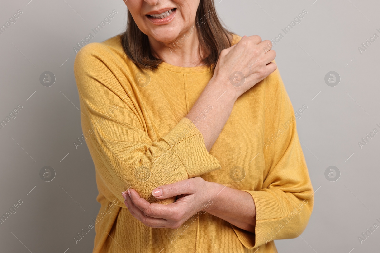 Photo of Arthritis symptoms. Woman suffering from pain in elbow on gray background, closeup