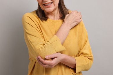 Arthritis symptoms. Woman suffering from pain in elbow on gray background, closeup