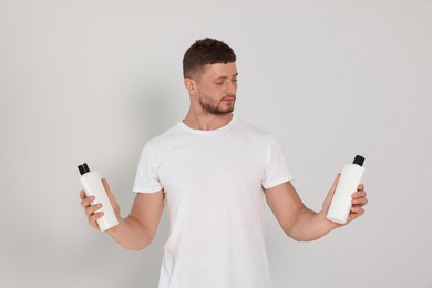 Photo of Handsome young man holding bottles of shampoo on white background