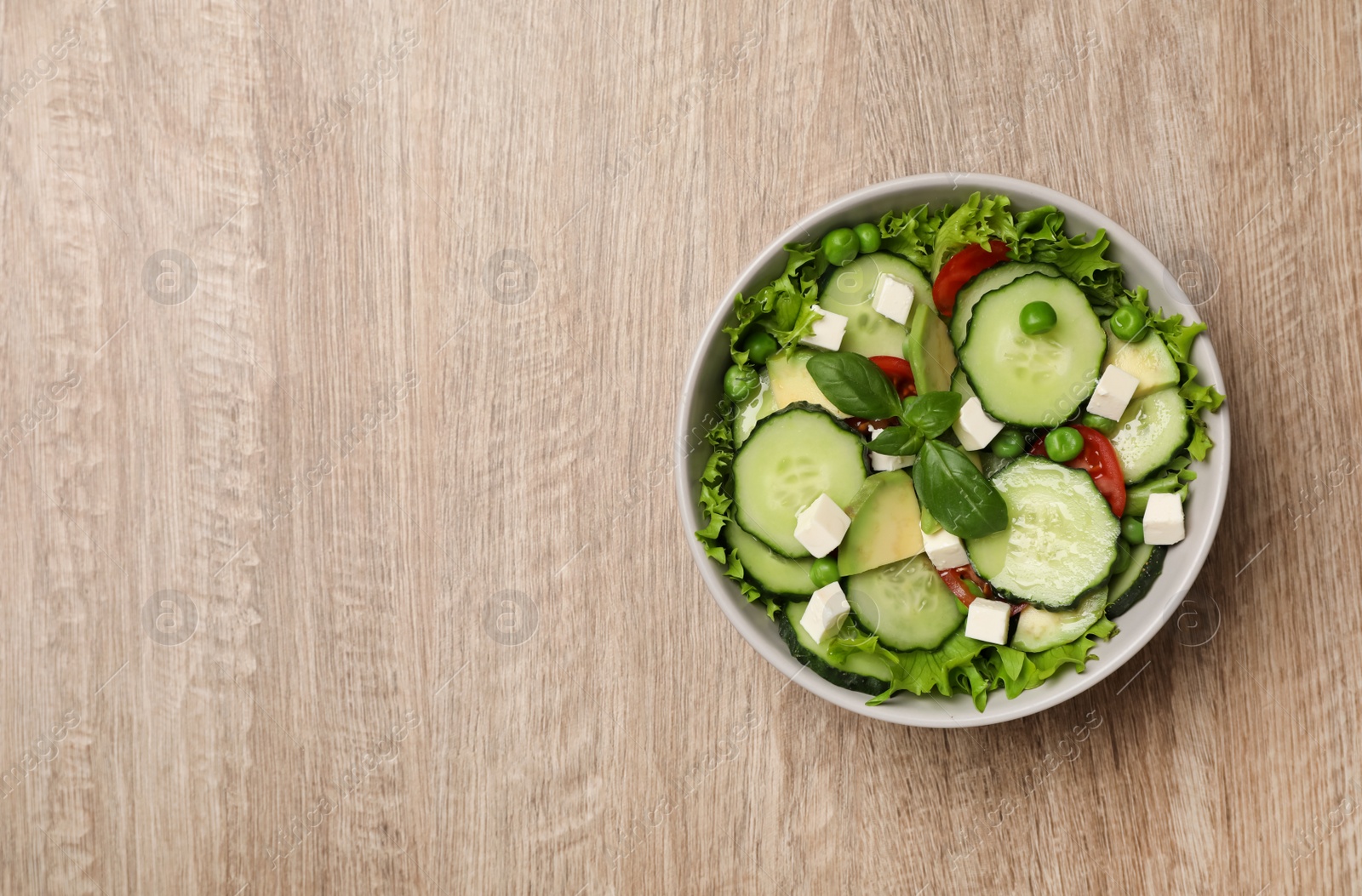 Photo of Tasty fresh salad with cucumber in bowl on wooden table, top view. Space for text