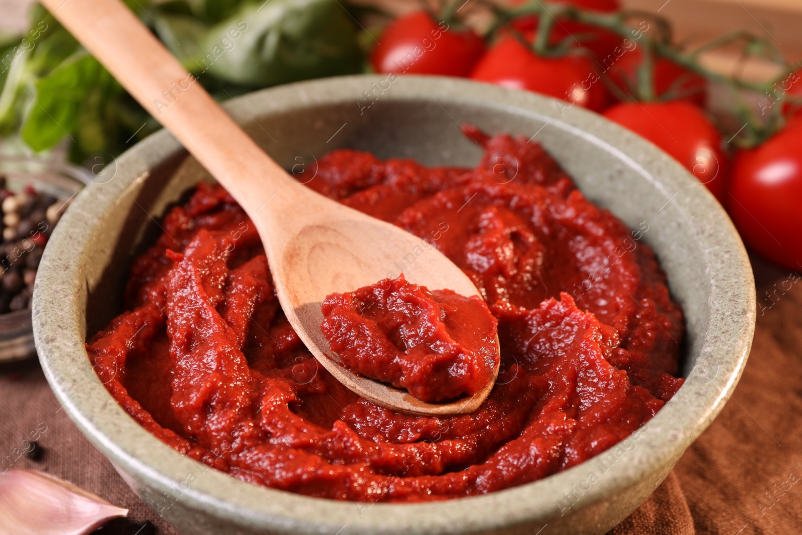 Photo of Bowl of tasty tomato paste with spoon and ingredients on table, closeup
