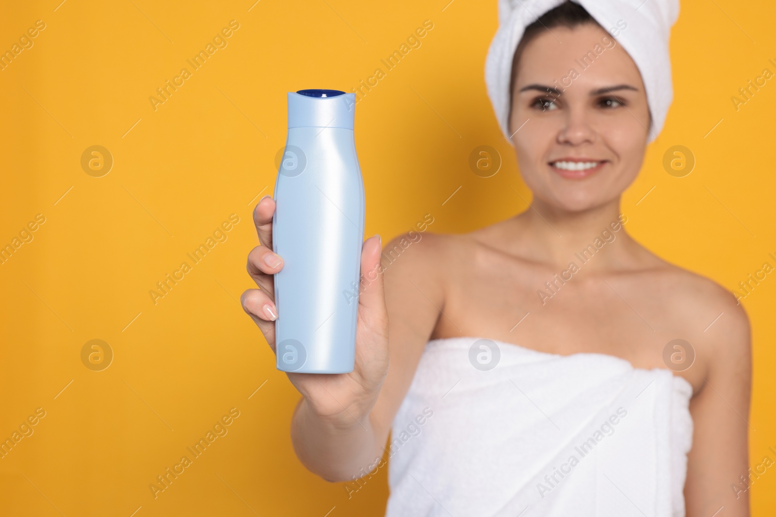 Photo of Beautiful young woman holding bottle of shampoo against orange background, focus on hand