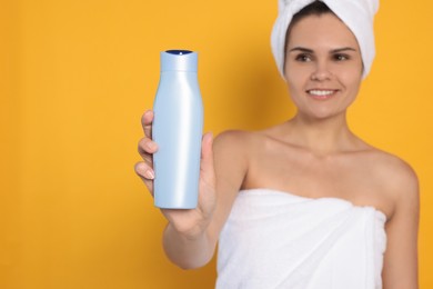 Photo of Beautiful young woman holding bottle of shampoo against orange background, focus on hand