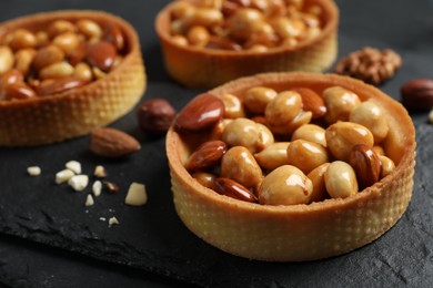Tartlets with caramelized nuts on black table, closeup. Delicious dessert