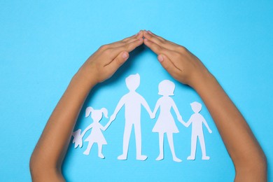 Child covering paper family figures with hands on light blue background, top view
