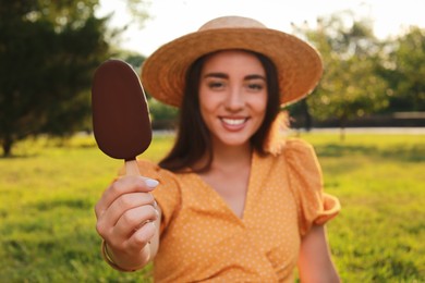 Beautiful young woman holding ice cream glazed in chocolate outdoors, focus on hand