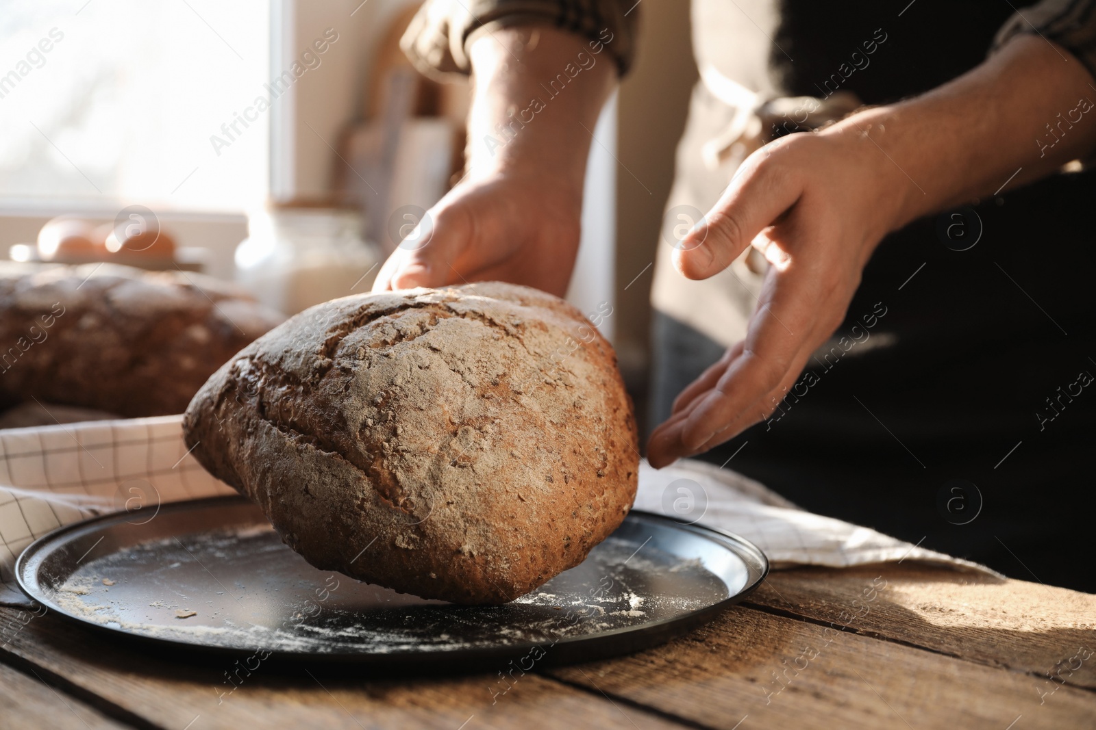 Photo of Man holding loaf of fresh bread at wooden table indoors, closeup