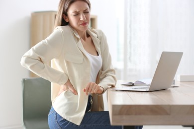 Photo of Woman suffering from back pain in office. Symptom of bad posture