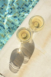 Glasses of tasty wine on swimming pool edge, top view