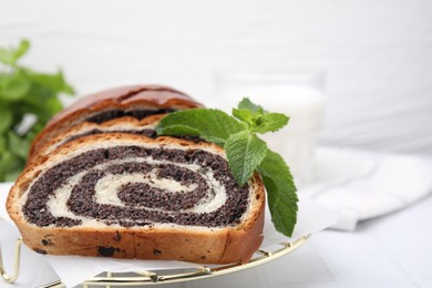 Photo of Slices of poppy seed roll and mint on white table, closeup with space for text. Tasty cake