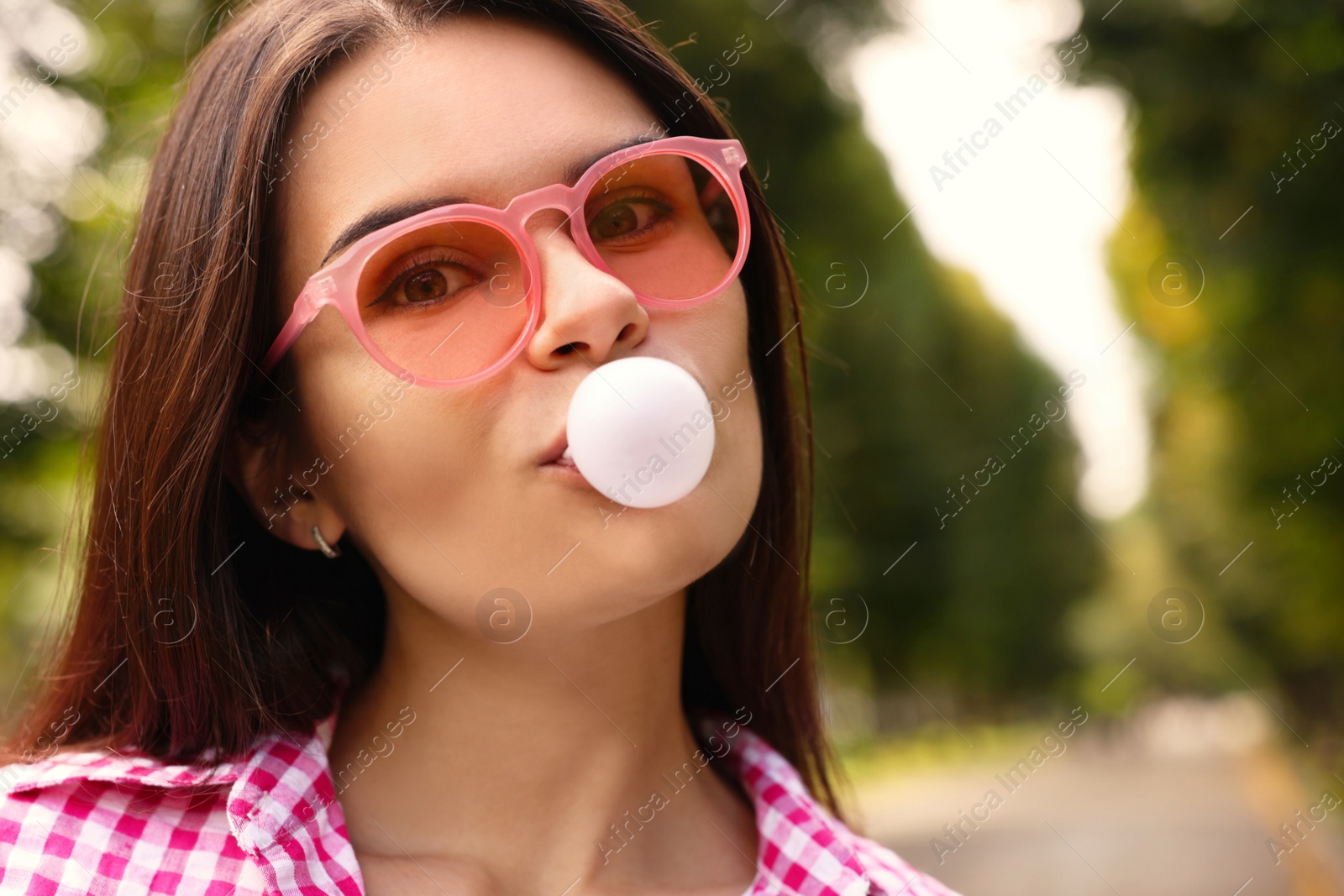 Photo of Beautiful young woman with pink sunglasses blowing chewing gum outdoors