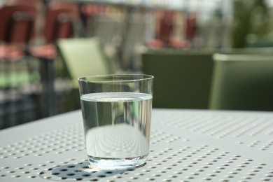 Photo of Glass of fresh water on white table outdoors. Space for text