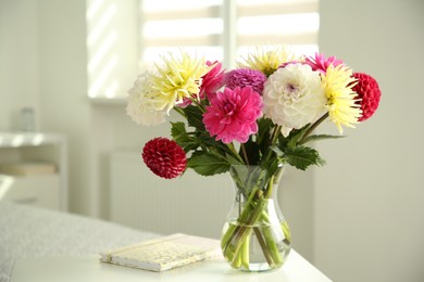 Photo of Bouquet of beautiful Dahlia flowers in vase and notebook on white table indoors. Space for text