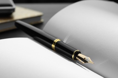 Photo of Stylish black fountain pen on open notebook, closeup