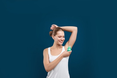Young woman applying deodorant to armpit on blue background