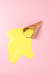 Melted ice cream and wafer cone on pink background, top view