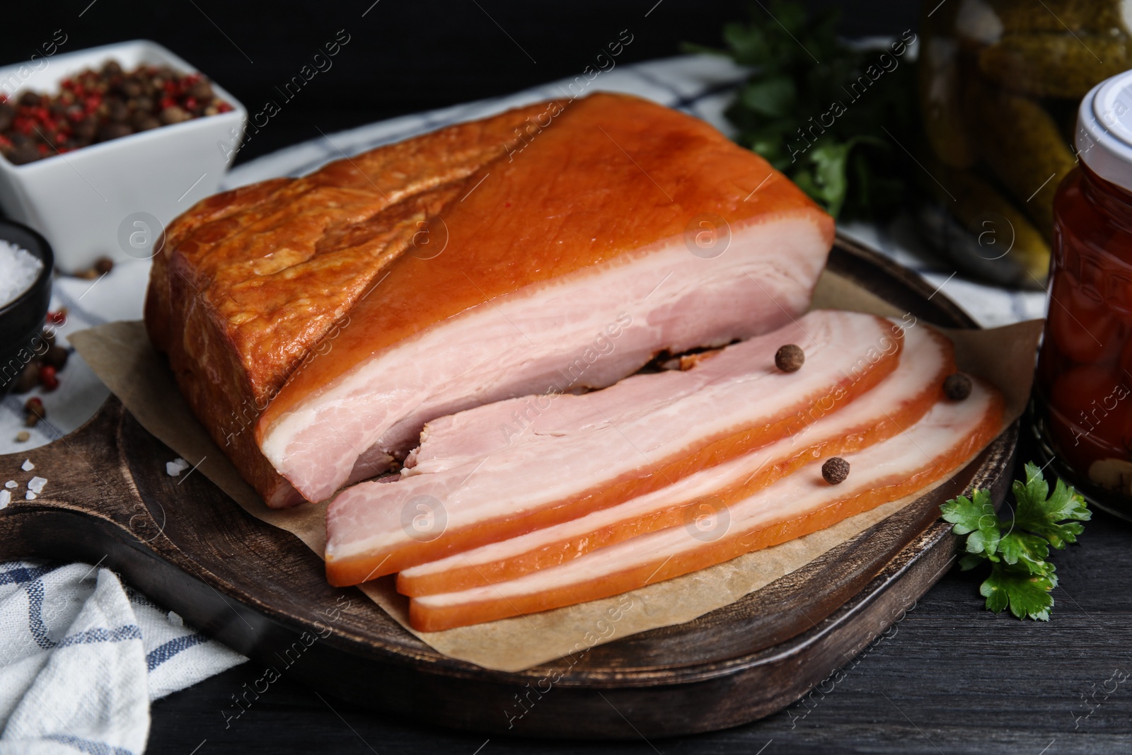 Photo of Delicious smoked bacon with spices and parsley on black wooden table, closeup