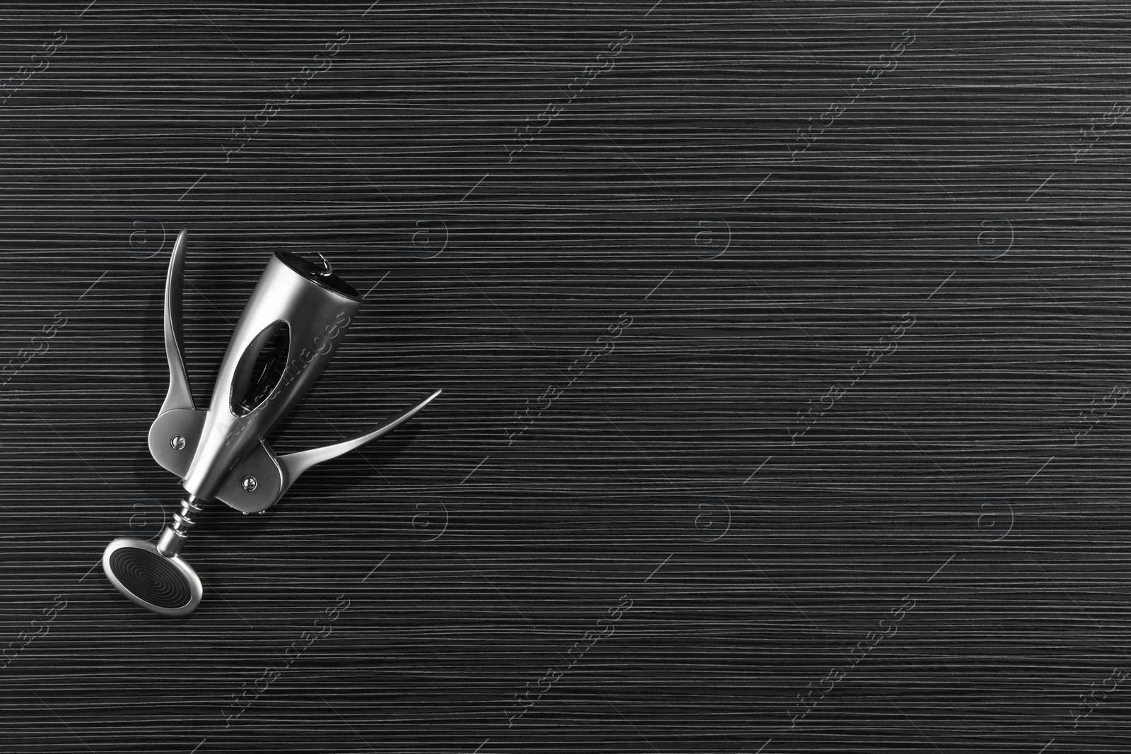 Photo of One wing corkscrew on black wooden table, top view. Space for text