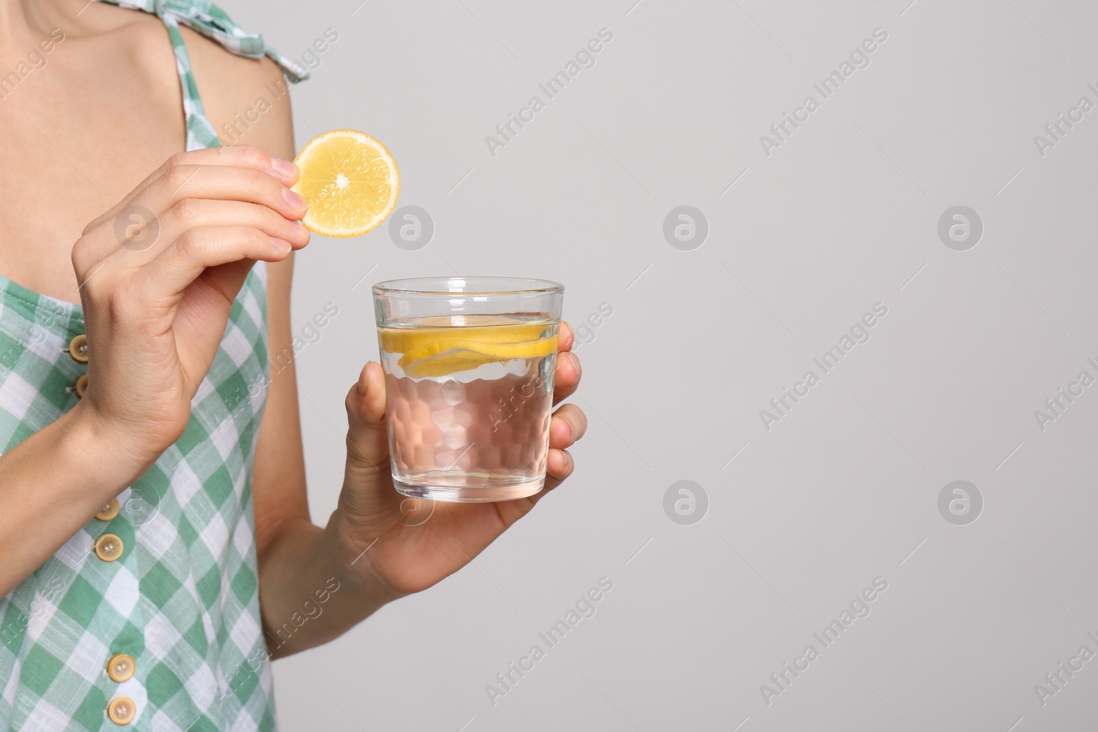 Photo of Young woman with glass of lemon water on light background, closeup. Space for text