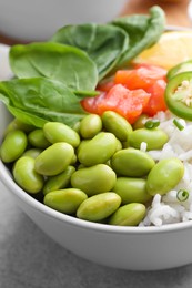 Photo of Poke bowl with salmon, edamame beans and rice on light grey table, closeup