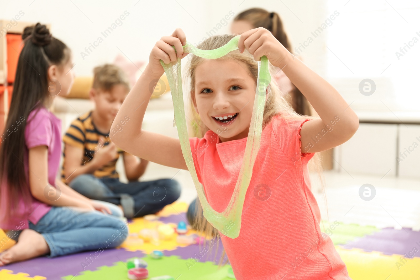 Photo of Happy little girl playing with slime in room