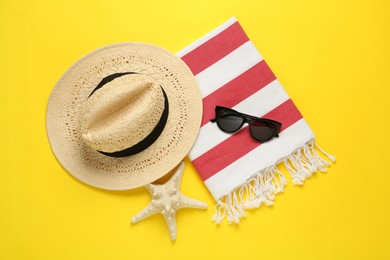 Beach towel, straw hat and sunglasses on yellow background, flat lay