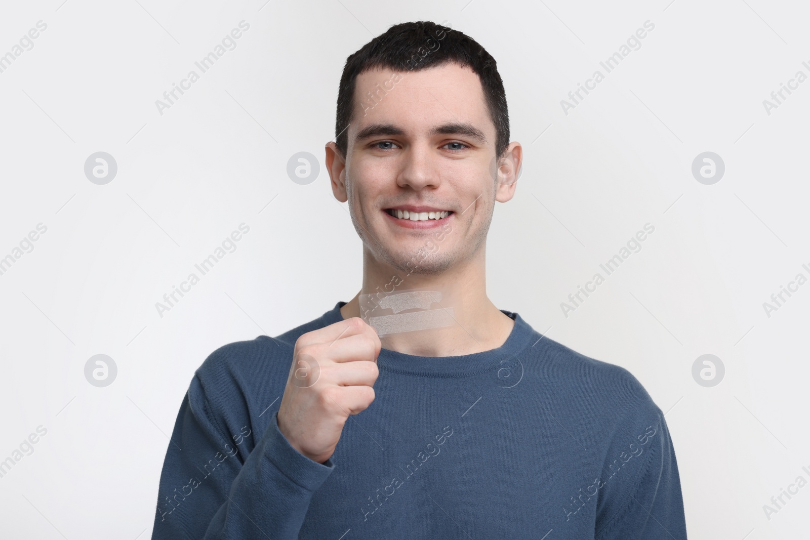 Photo of Young man with whitening strips on light background