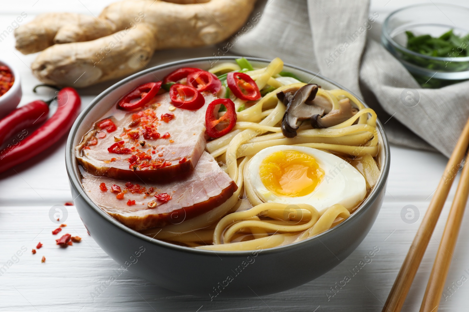 Photo of Delicious ramen in bowl and chopsticks on white wooden table, closeup. Noodle soup