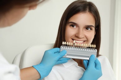 Photo of Doctor checking young woman's teeth color in clinic. Cosmetic dentistry