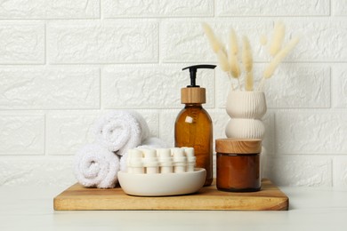 Different bath accessories, personal care products and spikelets in vase on white table near brick wall