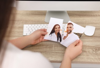 Photo of Woman holding torn photo at wooden table in room, closeup. Divorce concept