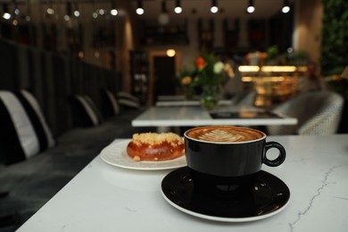Photo of Cup of fresh coffee and bun on table in cafeteria
