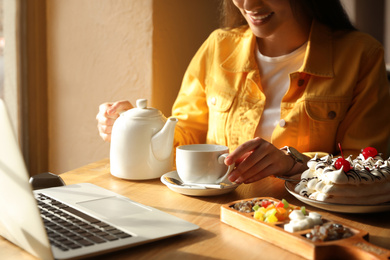 Photo of Young blogger pouring tea into cup at table in cafe, closeup