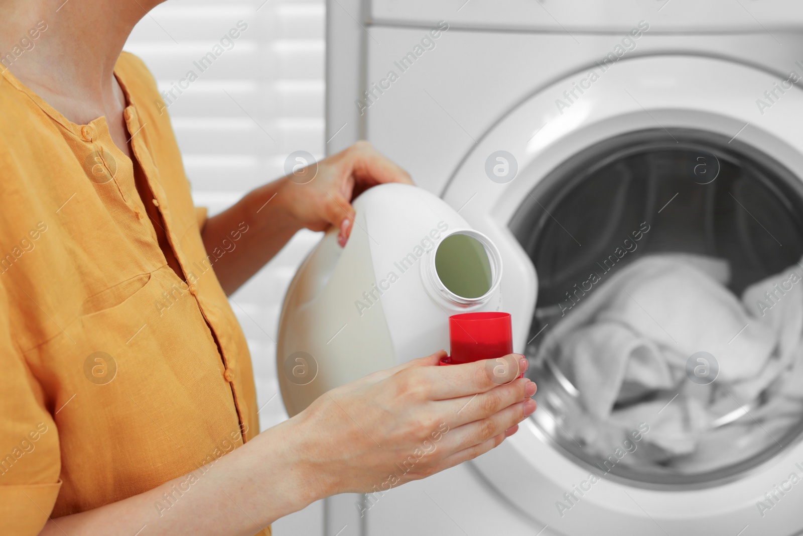 Photo of Woman pouring laundry detergent into cap near washing machine indoors, closeup. Space for text