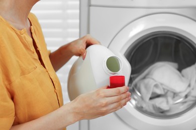 Photo of Woman pouring laundry detergent into cap near washing machine indoors, closeup. Space for text