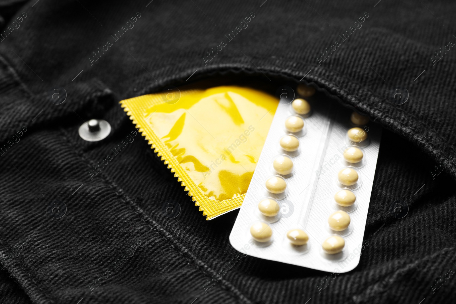 Photo of Yellow condom and birth control pills in pocket of jeans, closeup. Safe sex concept